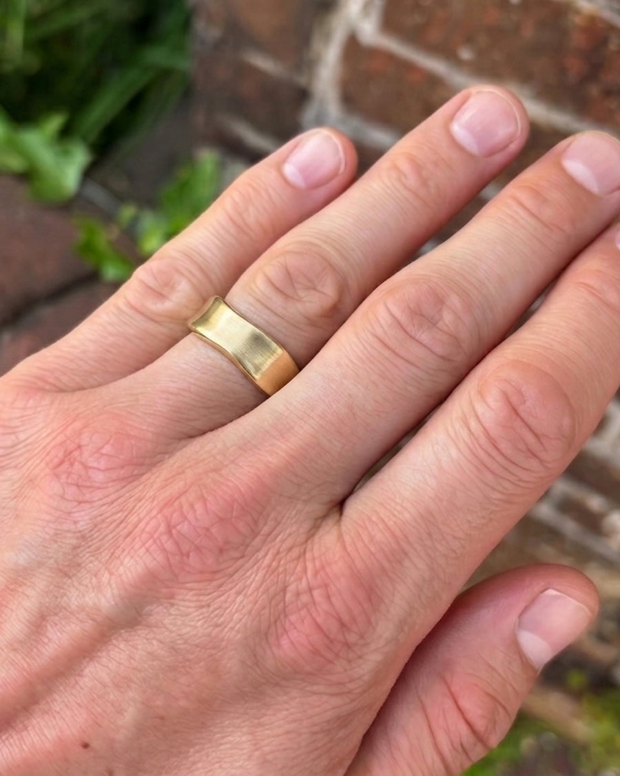 Men's gold side hammered brushed wedding ring on a hand.
