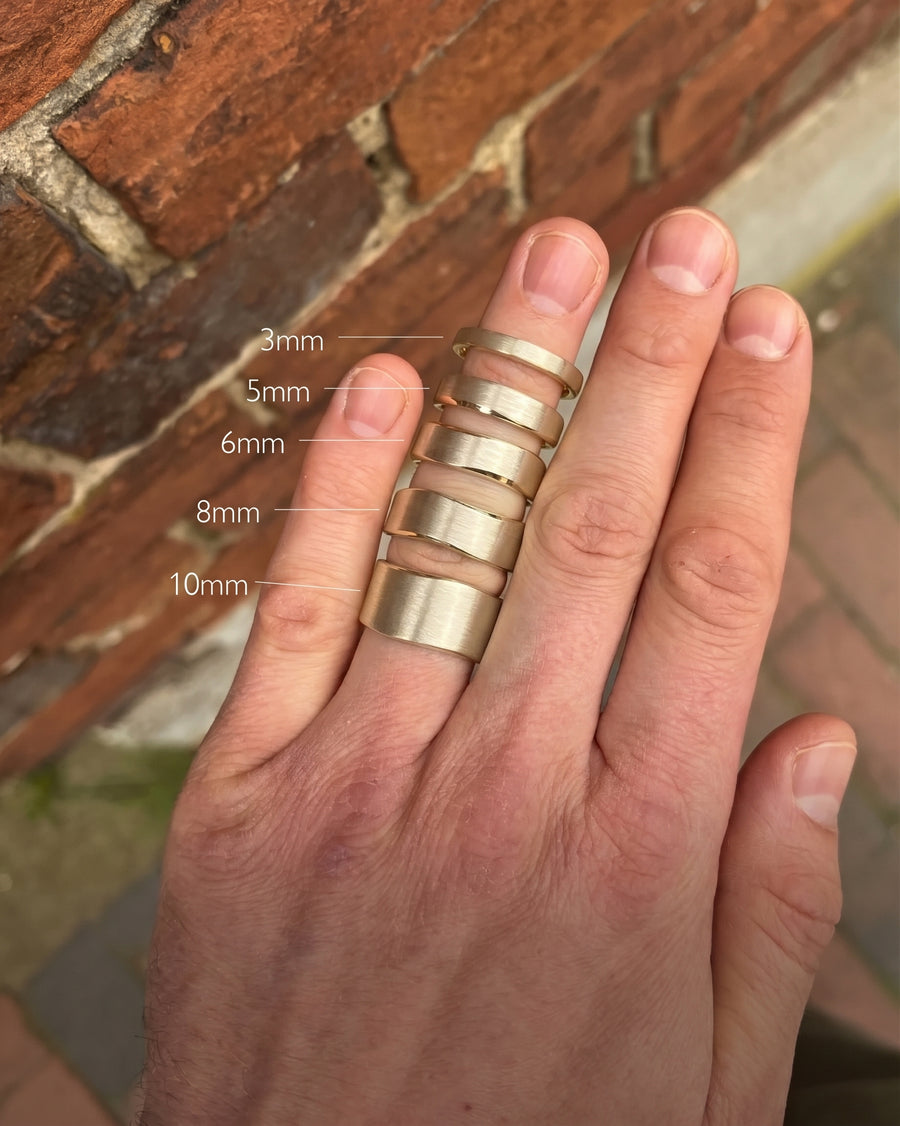 Brushed gold wedding rings in 3mm, 5mm, 6mm, 8mm, and 10mm widths on a hand.