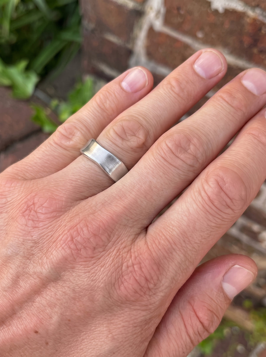 Silver-toned metal wedding ring with a brushed finish and hammered side details worn on a finger.