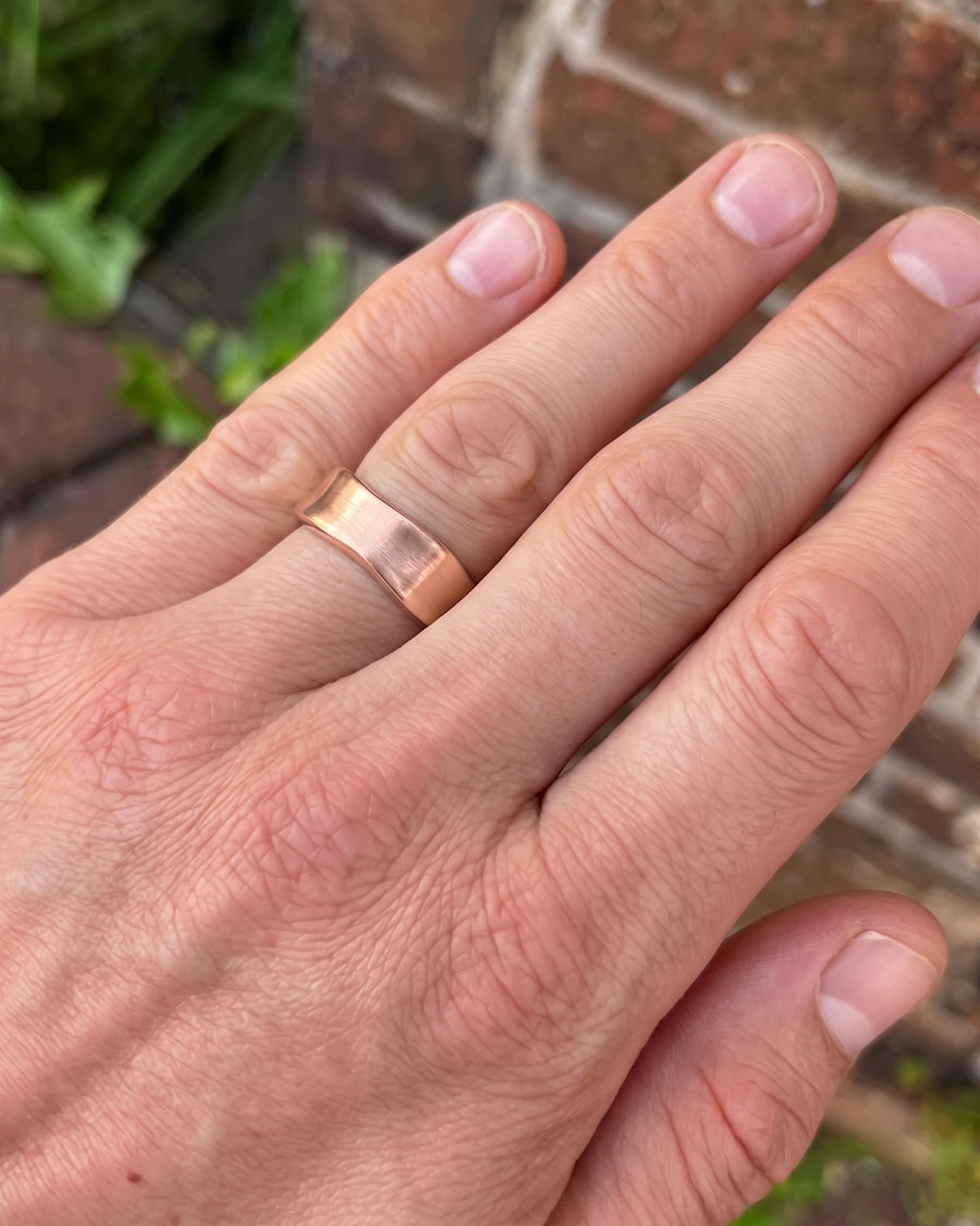 Rose gold wedding ring with a brushed finish and hammered side details worn on a finger.