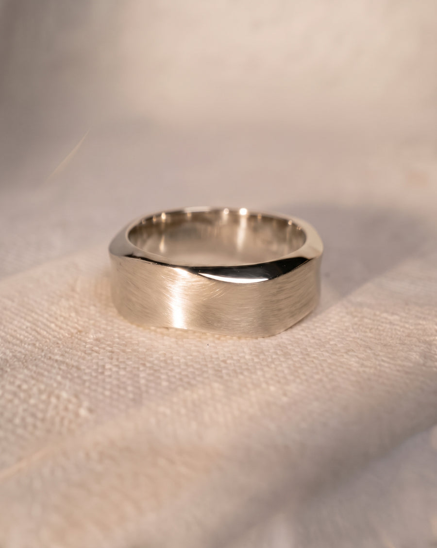 Silver wedding ring with a brushed finish and hammered side details resting on a textured fabric surface.