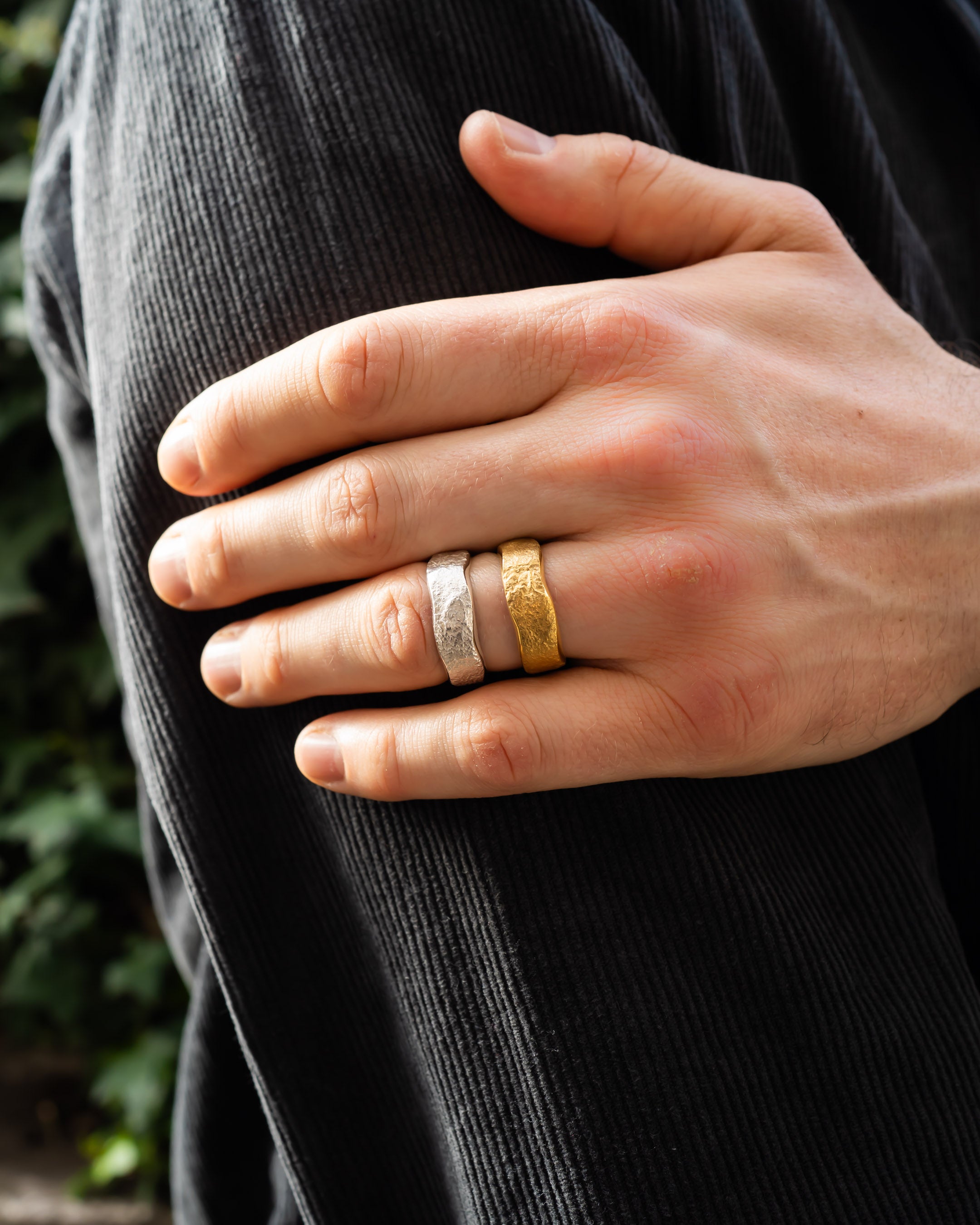 Hand wearing textured gold and silver wedding rings, close-up outdoors