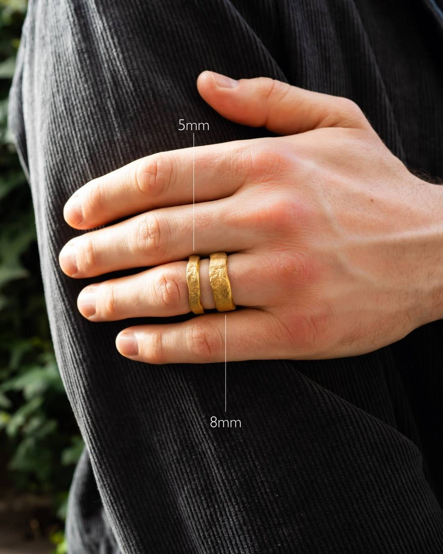 Two gold hammered textured men's wedding bands in 5mm and 8mm widths on hand