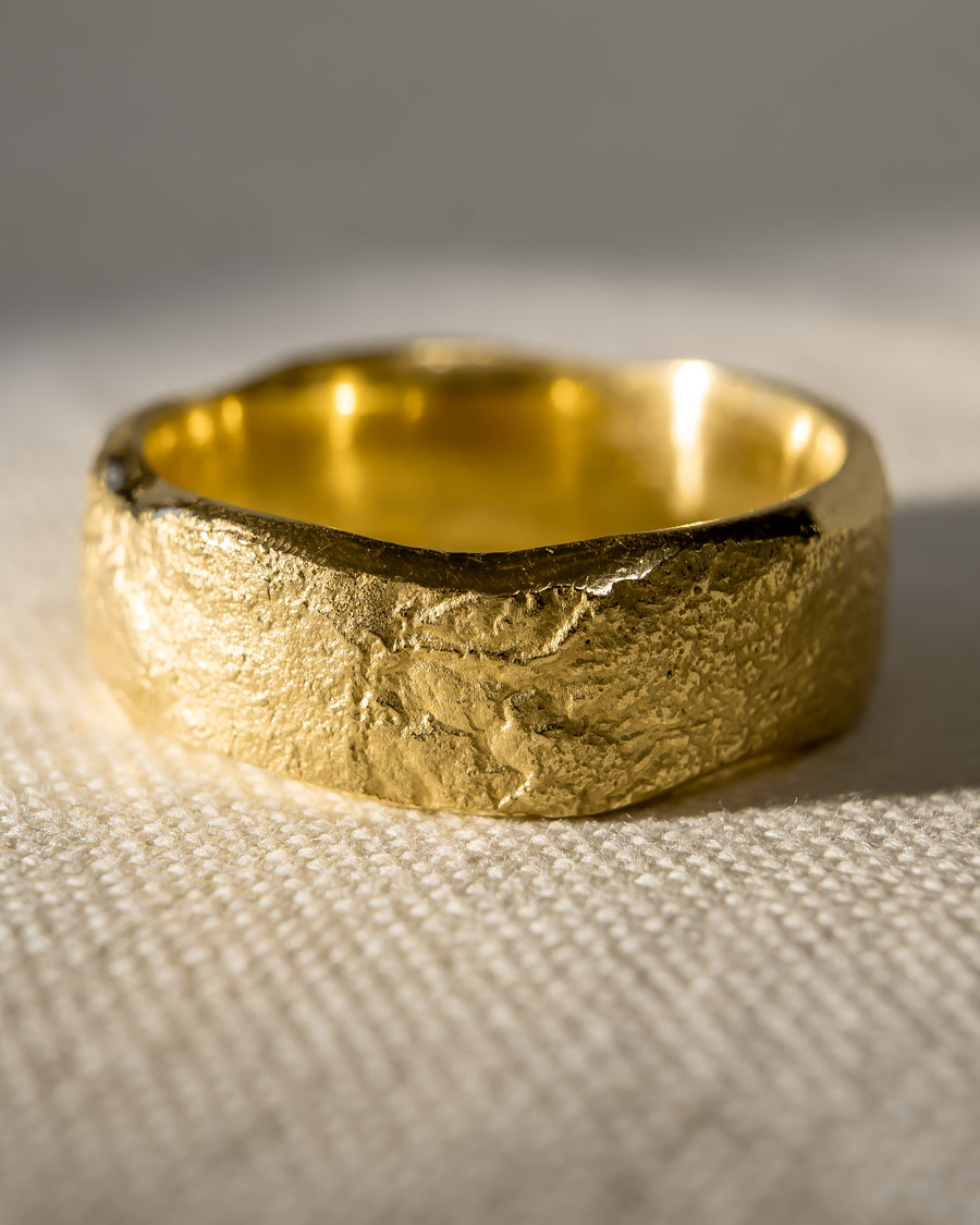 Textured gold wedding band with organic, rugged finish on a neutral fabric background
