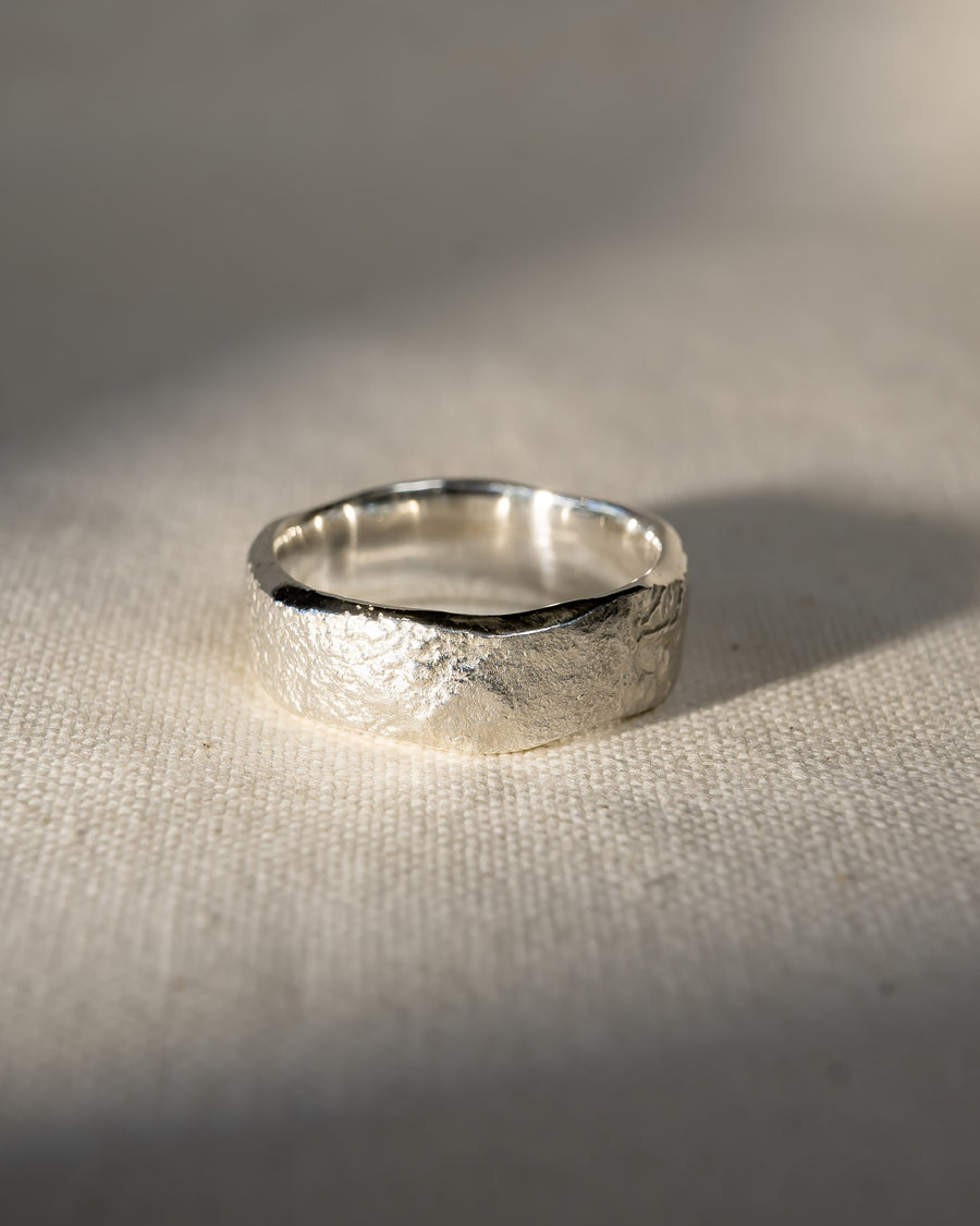 Handcrafted silver wedding ring with textured, organic finish on a natural fabric background