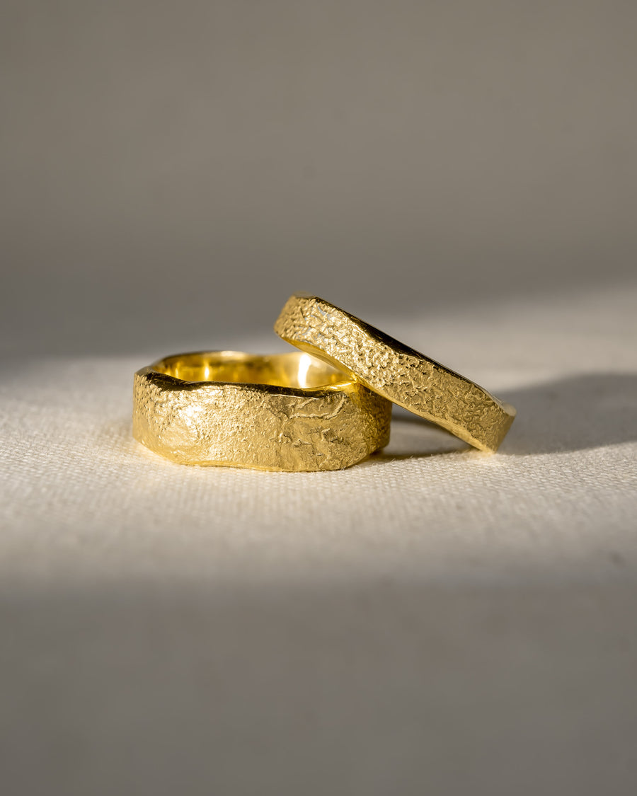 Two textured gold wedding rings with organic, handcrafted design on a neutral background