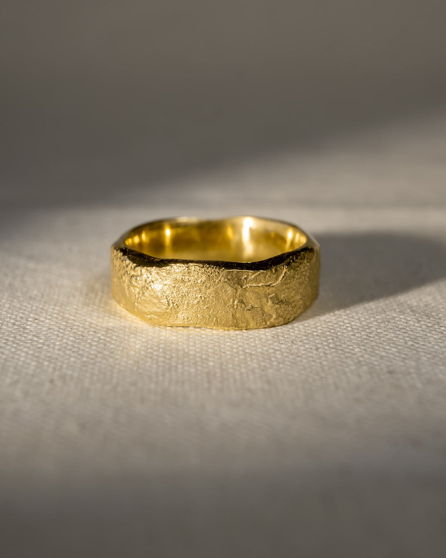 Textured gold wedding band with organic shape on a neutral fabric surface