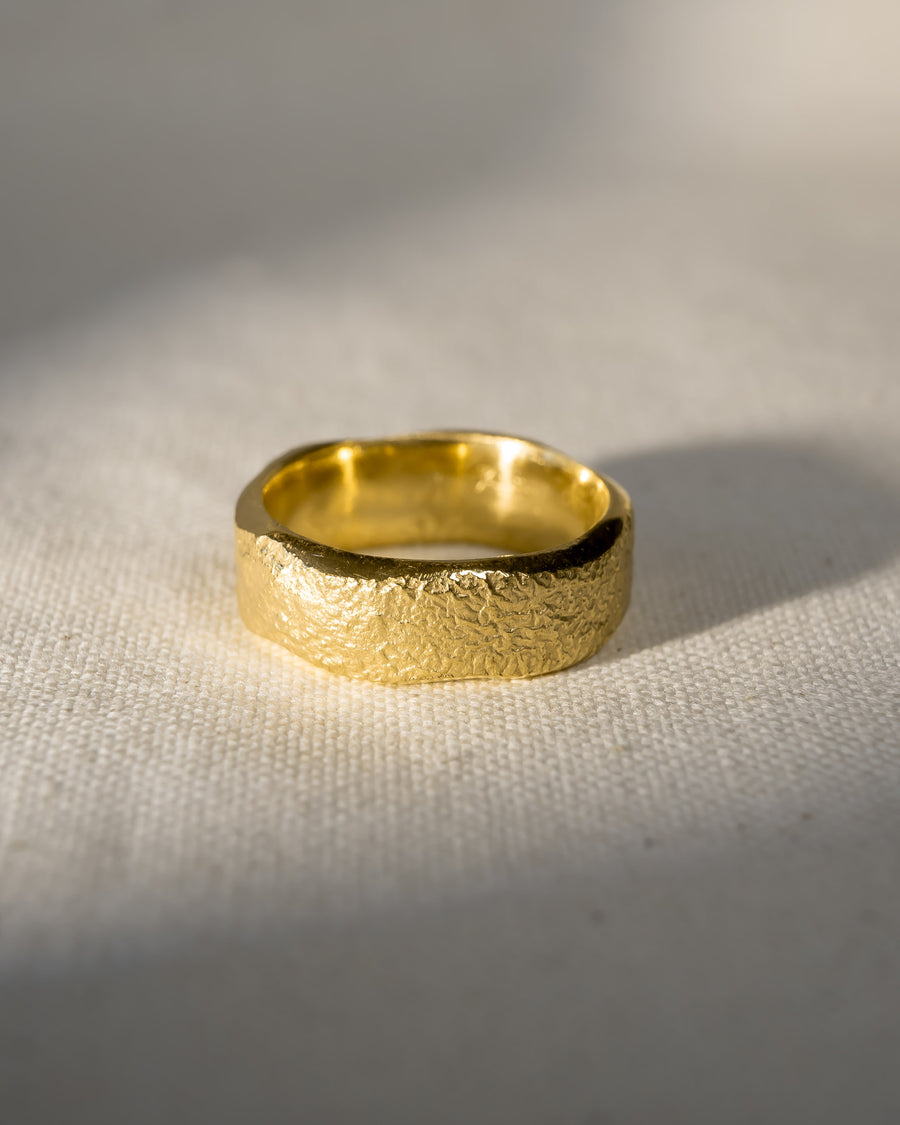 Handcrafted textured gold wedding ring on a light fabric background