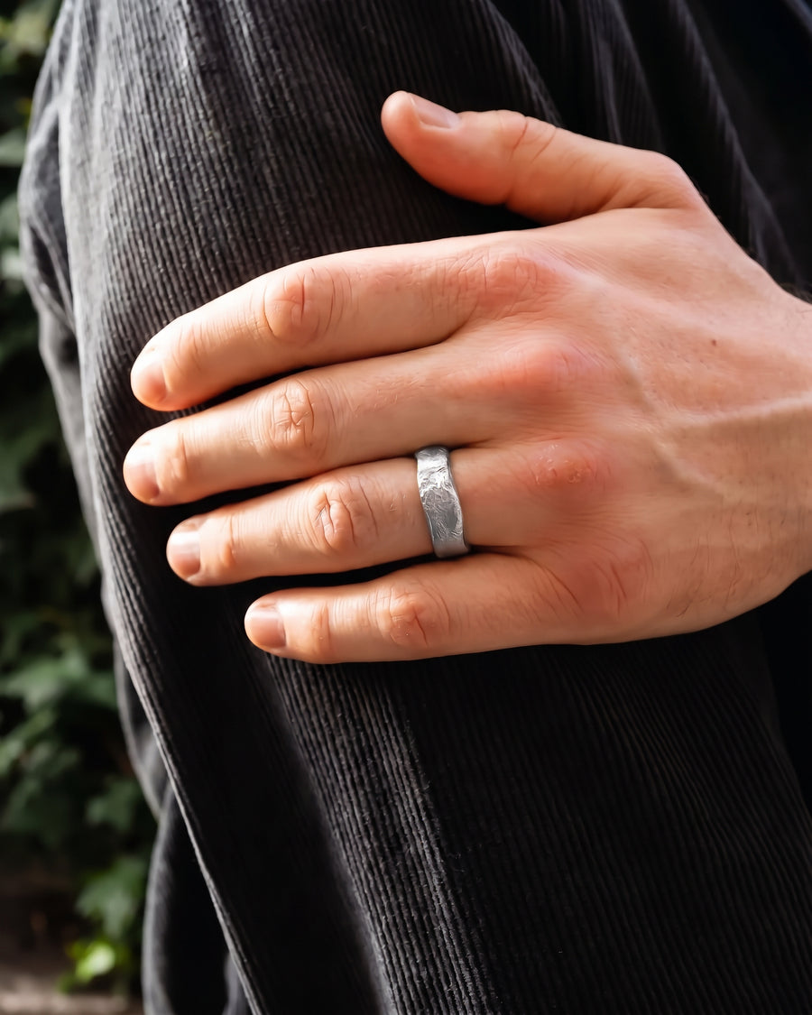 Silver wedding band with a textured, hammered finish worn on a man's finger.