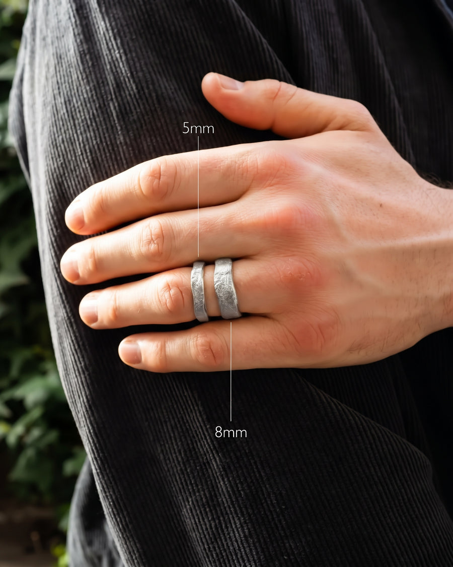 Silver wedding bands with a hammered texture, shown in 5mm and 8mm widths on a man's finger.
