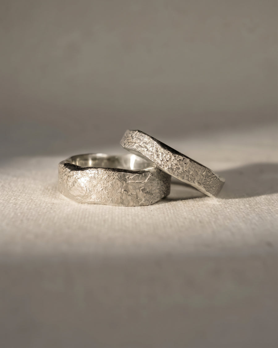 Two silver wedding bands featuring a textured, hammered finish resting on a light fabric surface.