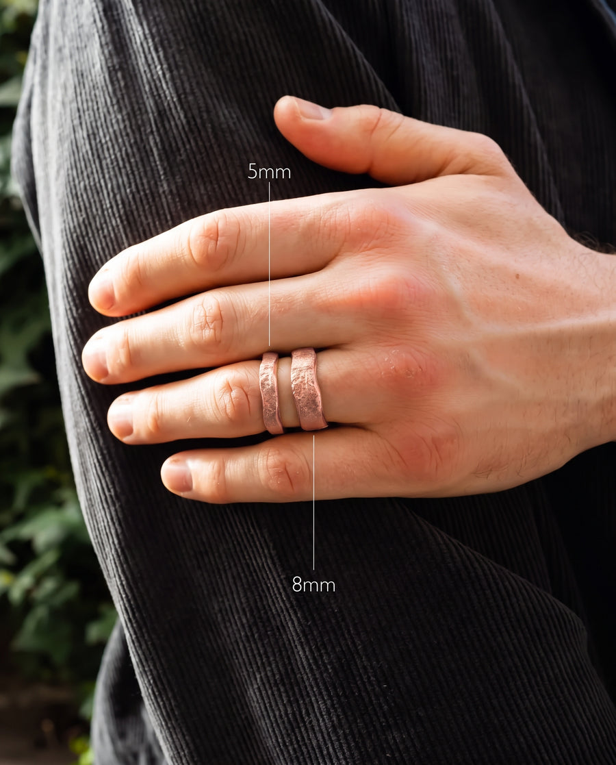 Two copper wedding bands with a hammered texture worn on a hand, showing 5mm and 8mm width options.