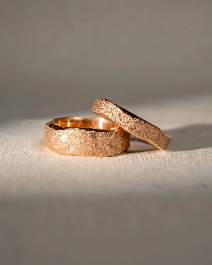 Two rose gold wedding bands with a hammered, textured finish resting on a light fabric surface.