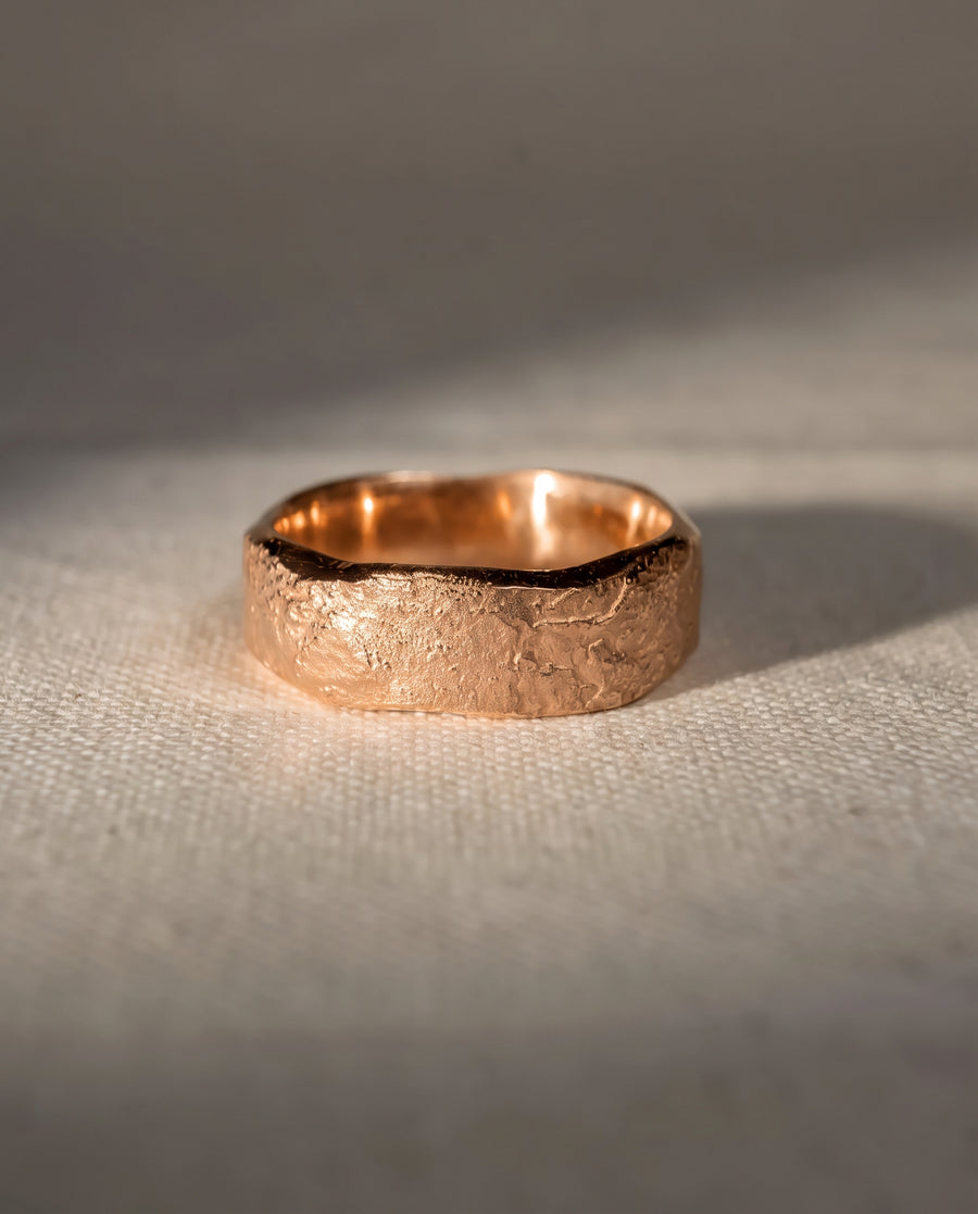 4mm 9ct rose gold wedding band with a textured, hammered finish sitting on a neutral fabric surface.