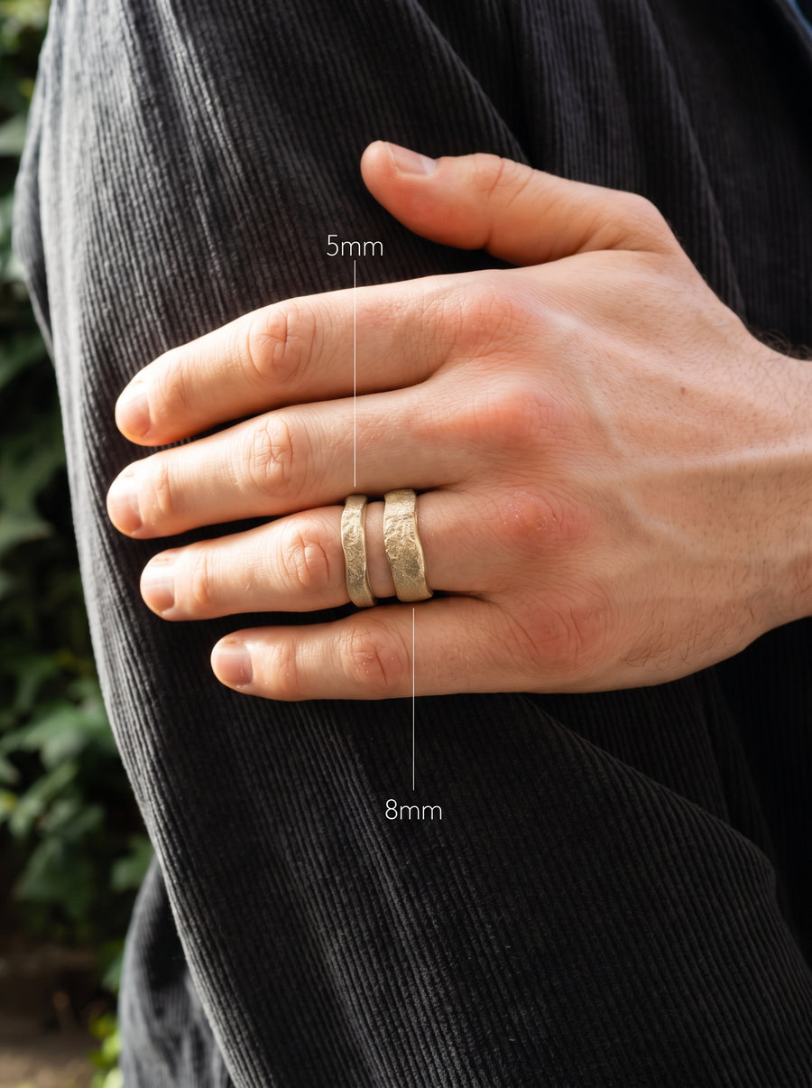 Two gold wedding bands with a hammered texture, shown in 5mm and 8mm widths on a man's finger.