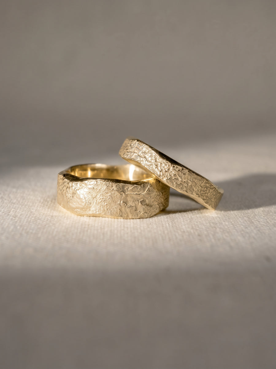 Two gold wedding bands with a hammered, textured finish resting on a light fabric surface.