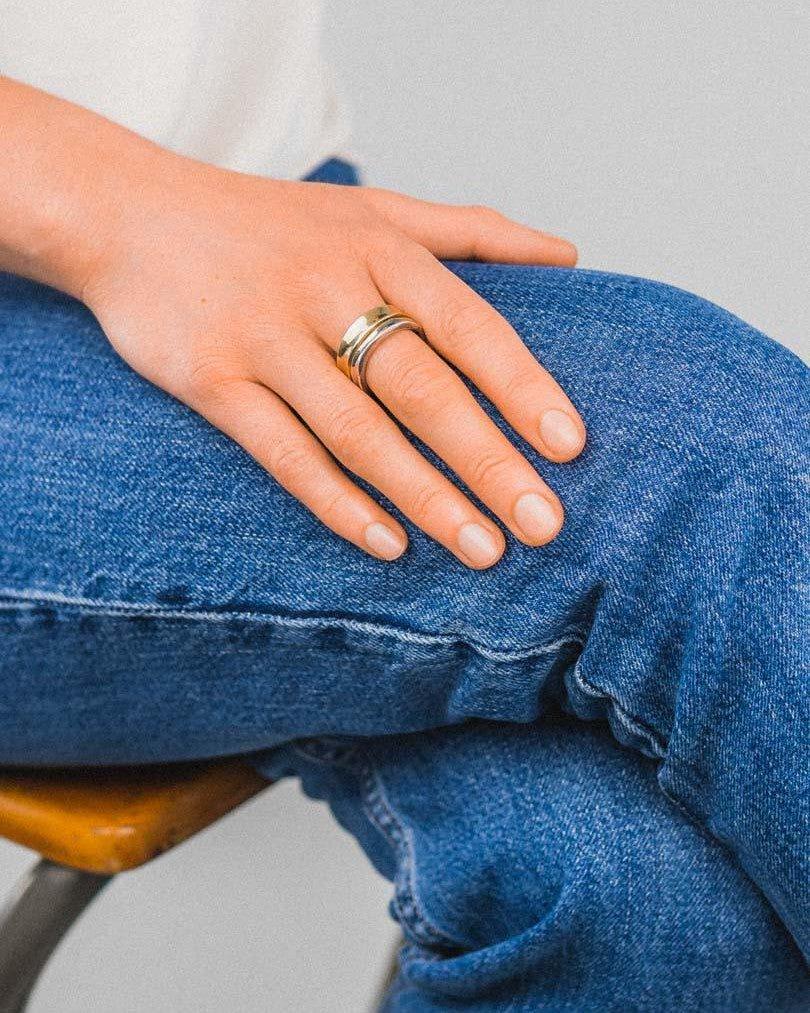 Hand wearing a hammered two-colour gold wedding ring, resting on blue jeans.