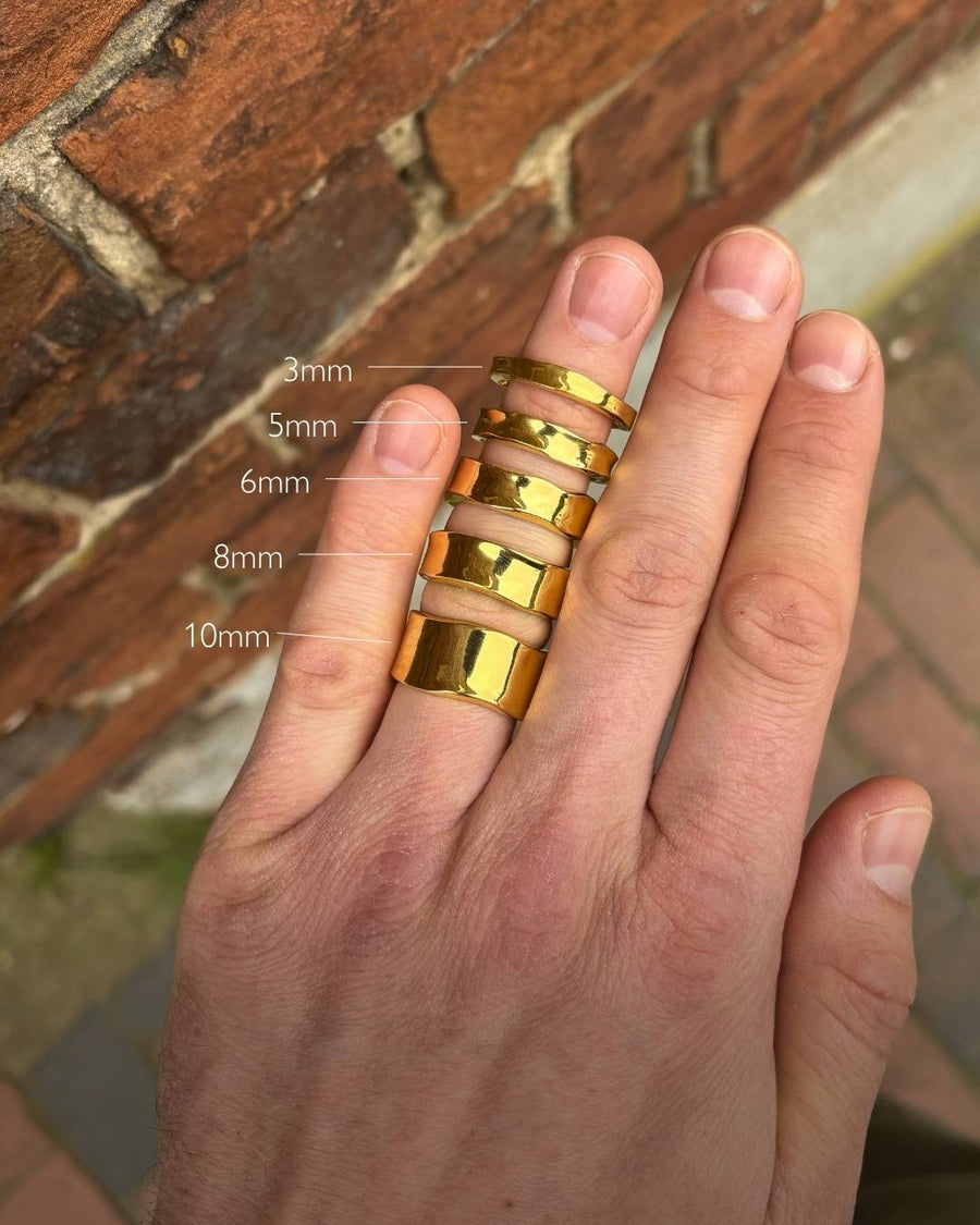 Gold-colored hammered wedding rings in 3mm, 5mm, 6mm, 8mm, and 10mm widths on a hand.
