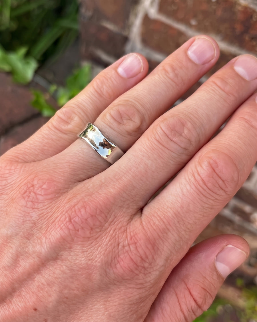 Polished silver wedding band with a curved, concave design worn on a finger.