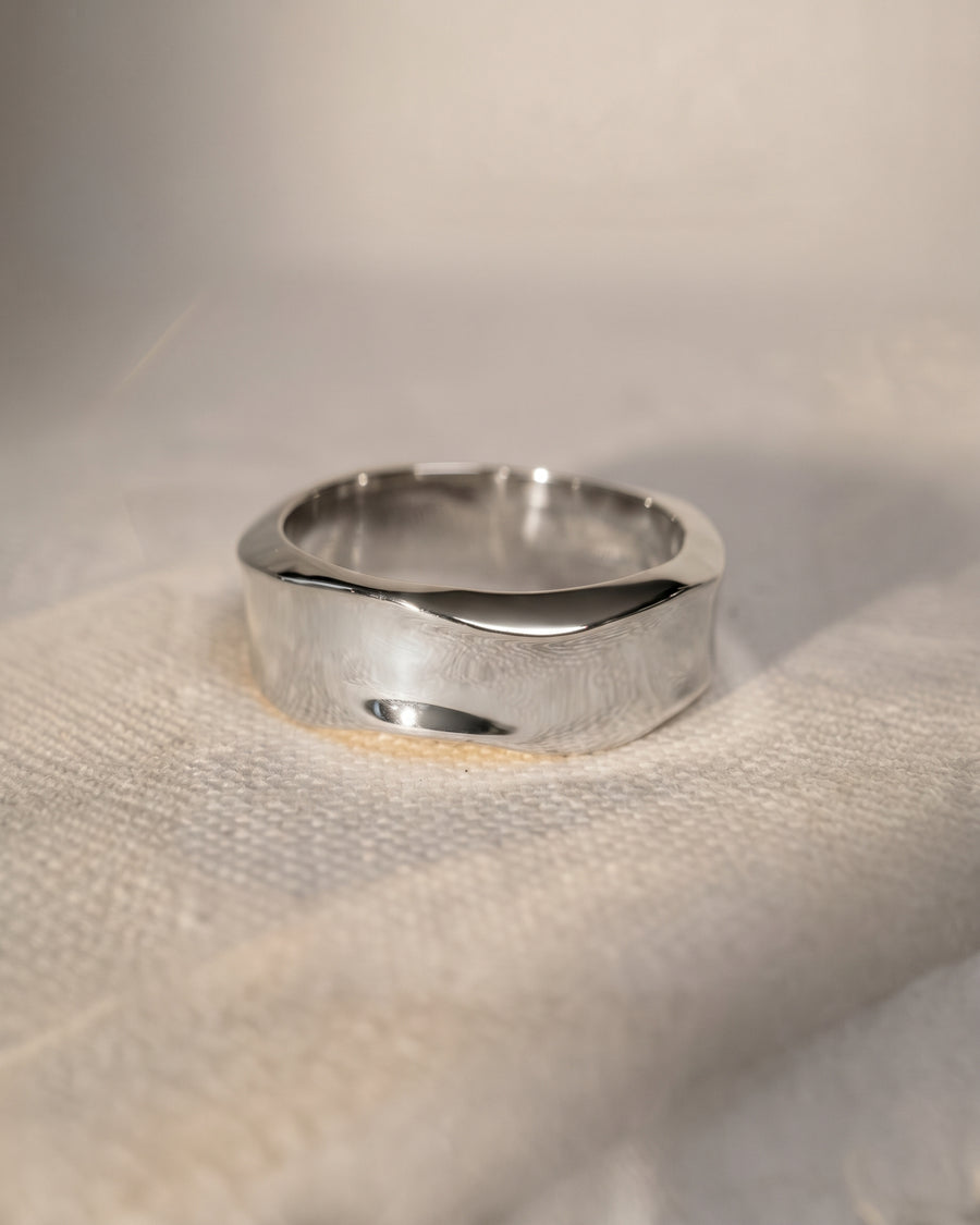 Polished silver men's wedding ring with a wide band and subtle hammered texture on the sides.