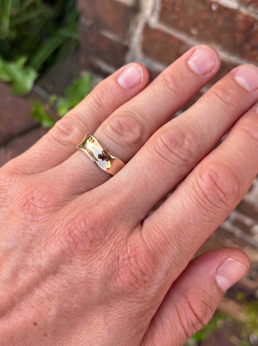Polished gold wedding ring with a wavy, hammered side design worn on a finger.