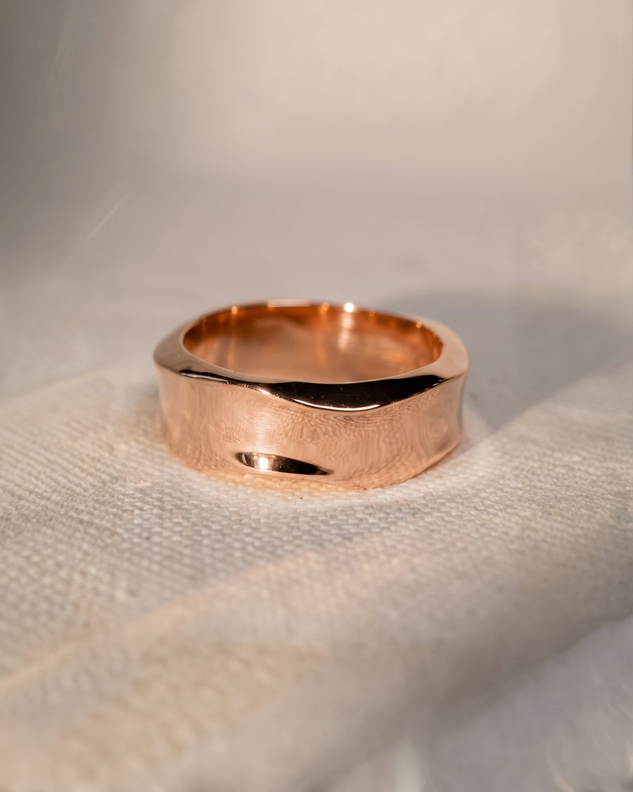 Rose gold wedding ring with a wide band and a textured, hammered side finish on a white surface.