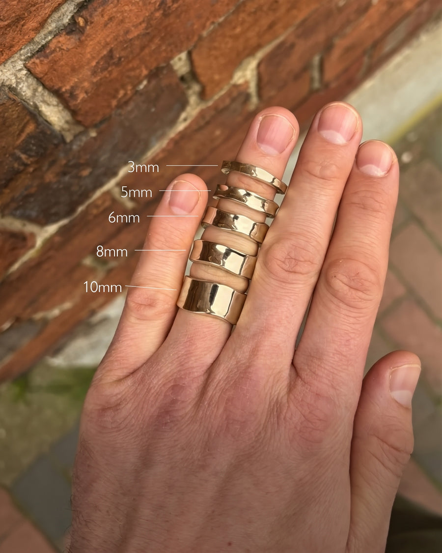 Gold wedding rings with hammered side textures in 3mm to 10mm widths worn on a hand.