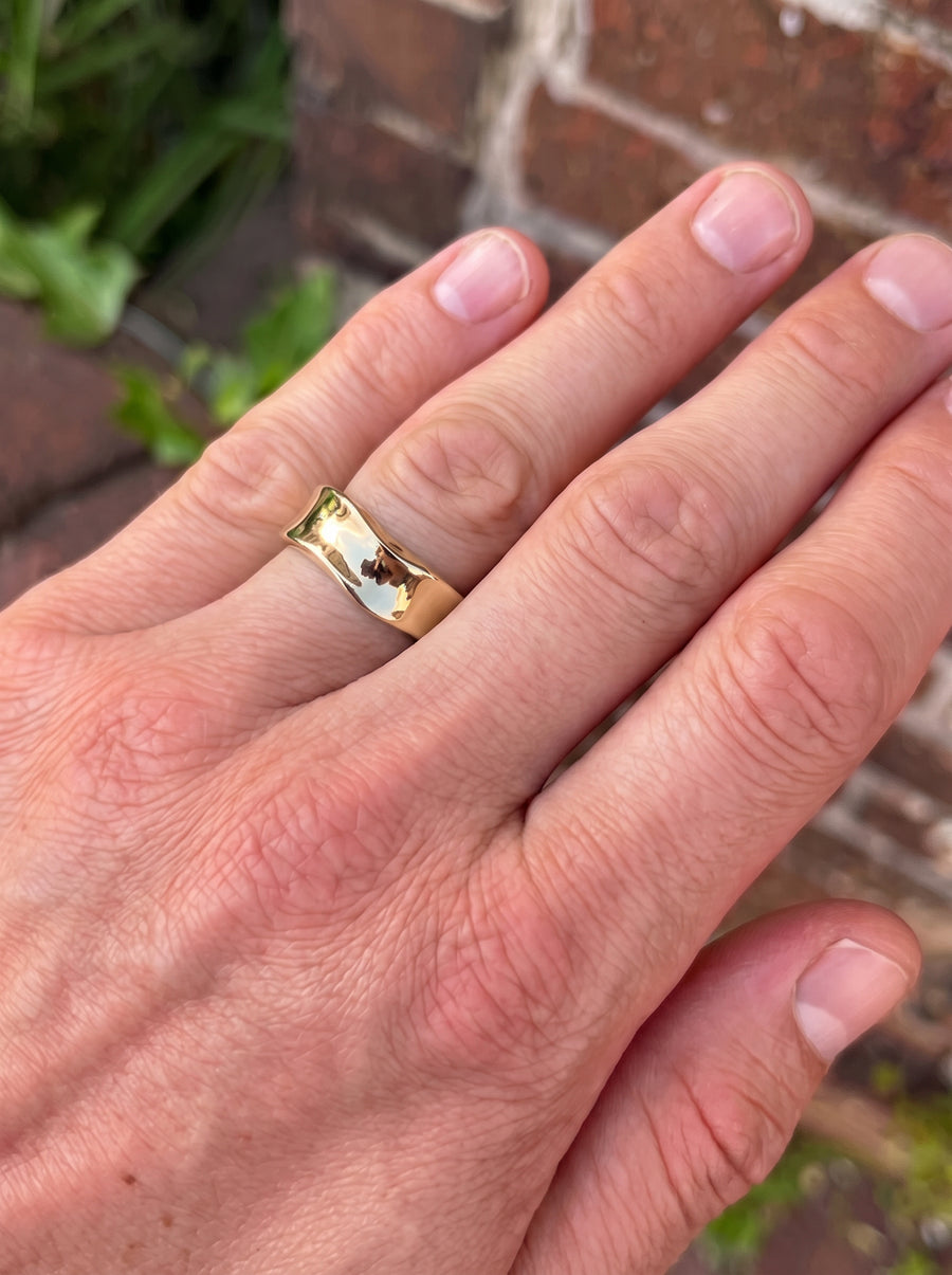Gold wedding band with a polished, hammered side finish worn on a finger.