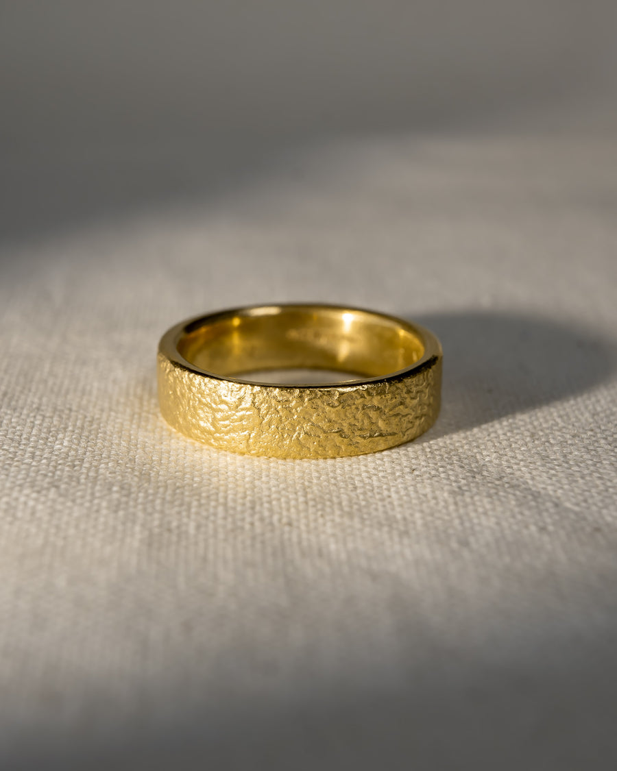 Textured gold wedding band with a matte finish on a neutral fabric background