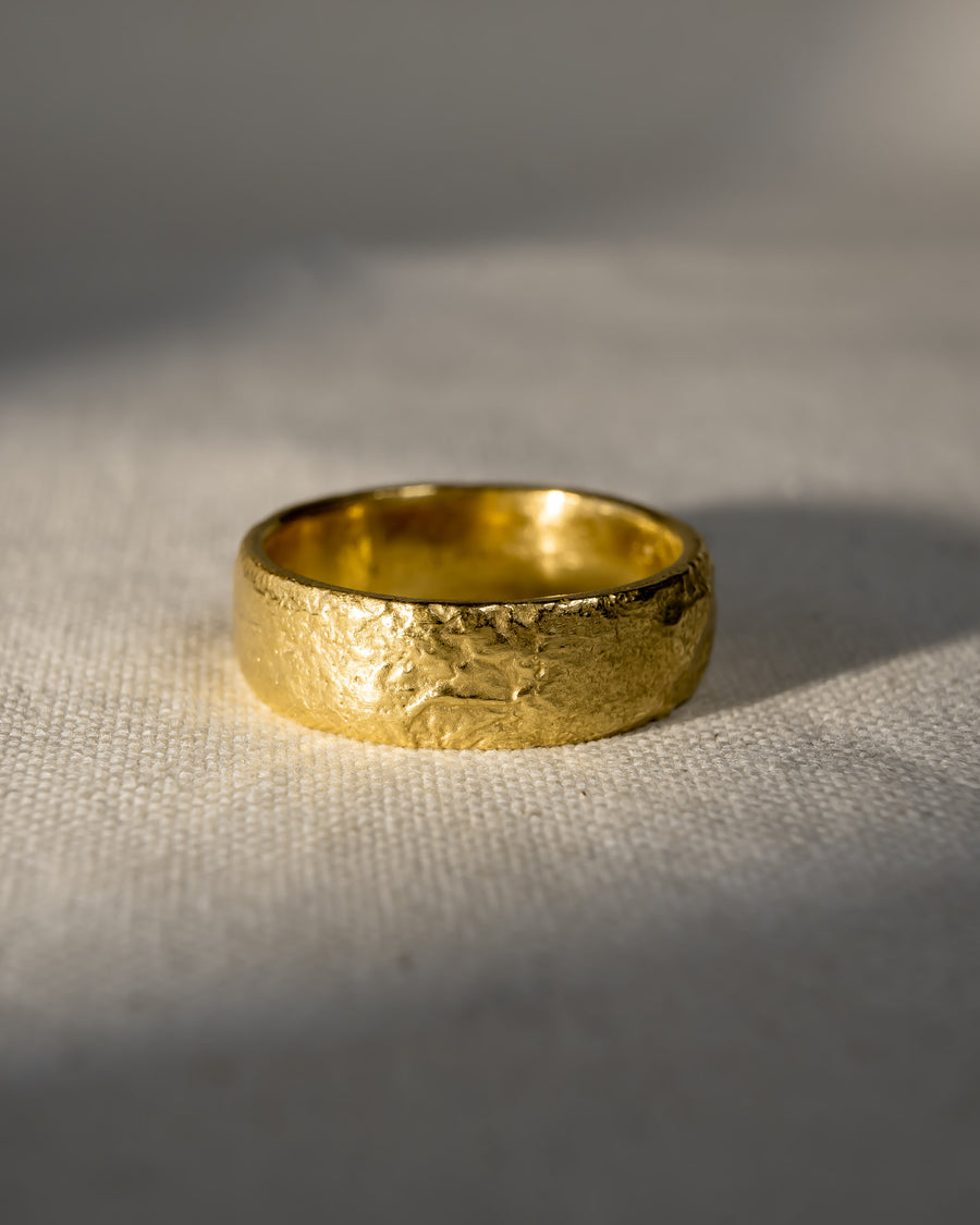 Textured gold wedding ring with organic, handmade finish on a neutral fabric background