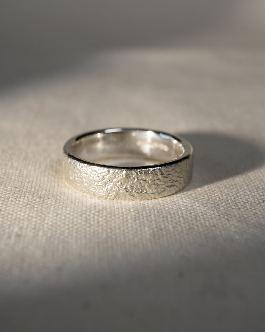 Textured silver wedding ring with organic finish on a cream fabric surface