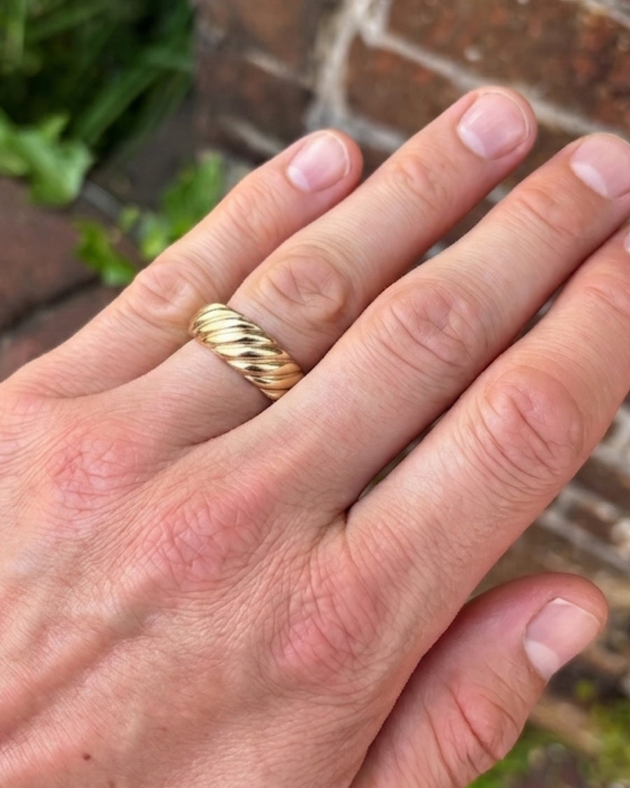 Yellow gold wedding band on a finger featuring a polished, twisted rope design.