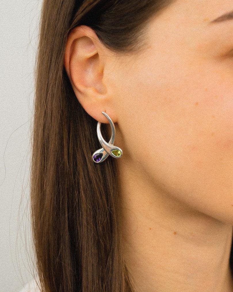 Silver drop earrings with peridot and amethyst gemstones worn on ear, handmade luxury jewellery
