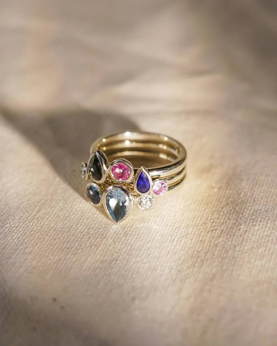 Gold stacking rings with multi-coloured aquamarine and sapphire pear gemstones.