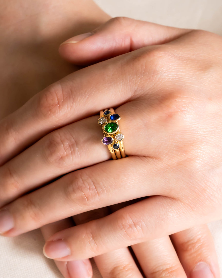 Gold stacking rings with multi-coloured oval sapphires and diamonds on a hand.