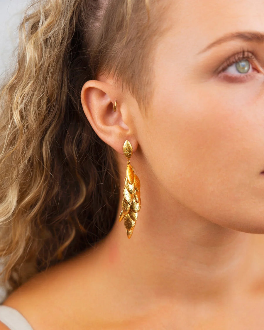 Gold multi-leaf long drop earrings on a woman's ear.
