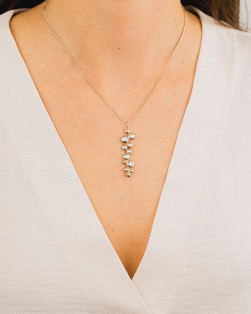 Yellow gold pendant with diamonds on a delicate chain, worn with a light v-neck top