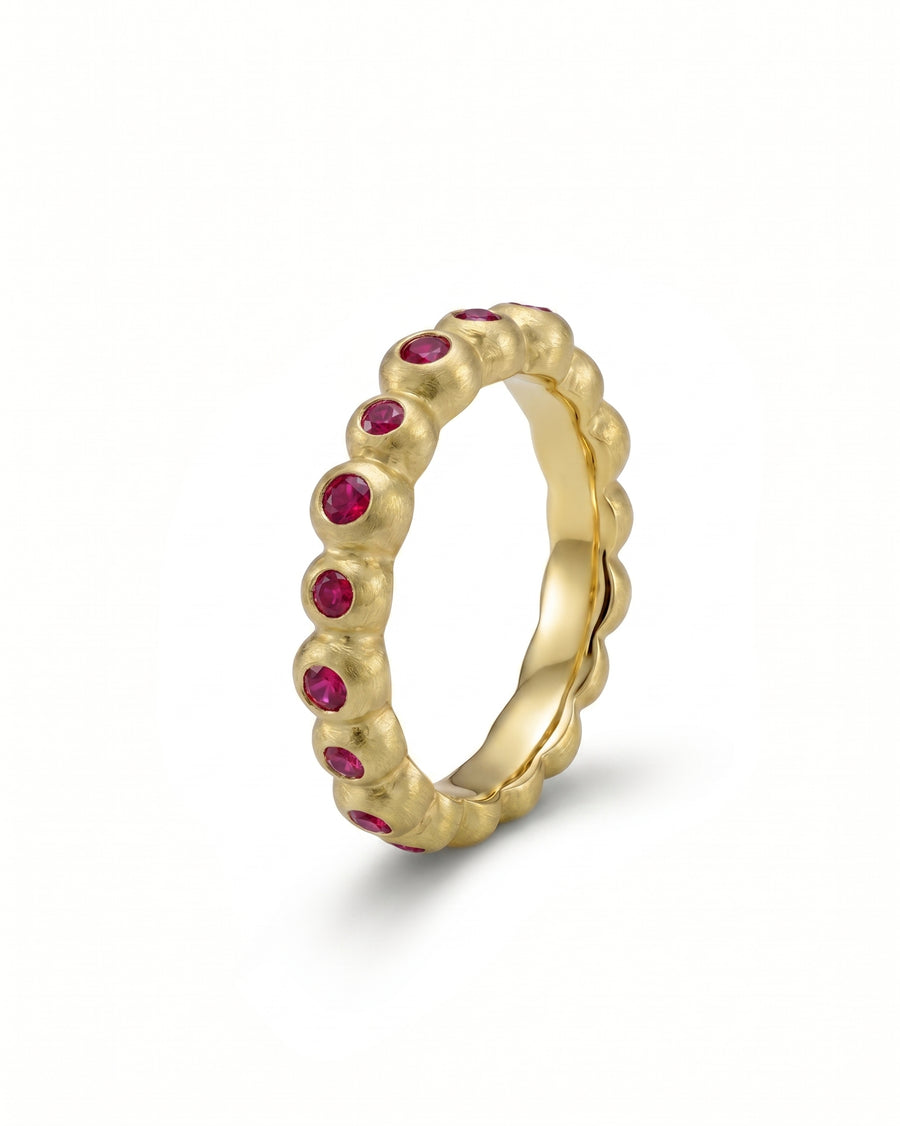 Yellow gold eternity ring with round red gemstones in a nugget-style band.