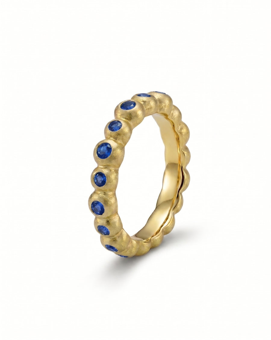 Yellow gold eternity ring with blue sapphire gemstones.
