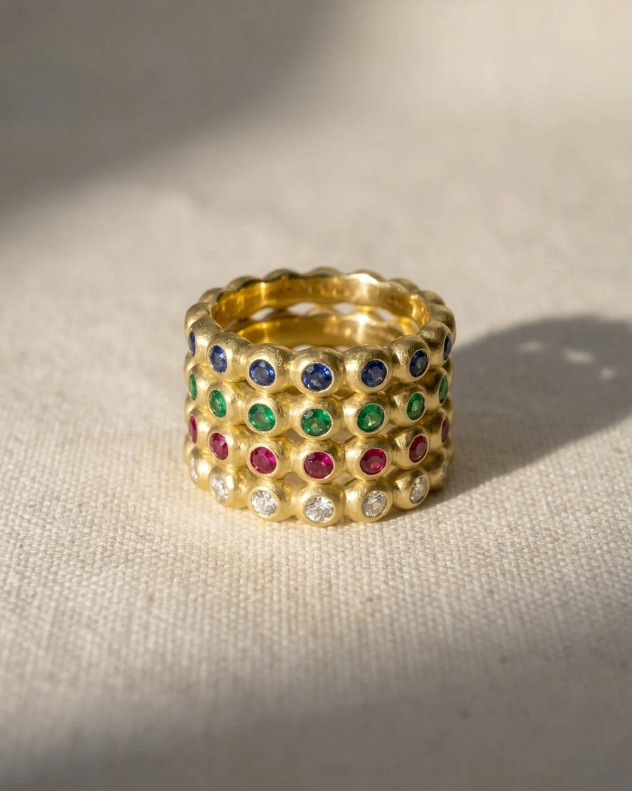 Yellow gold nugget eternity rings with blue, green, red gemstones, and diamonds.
