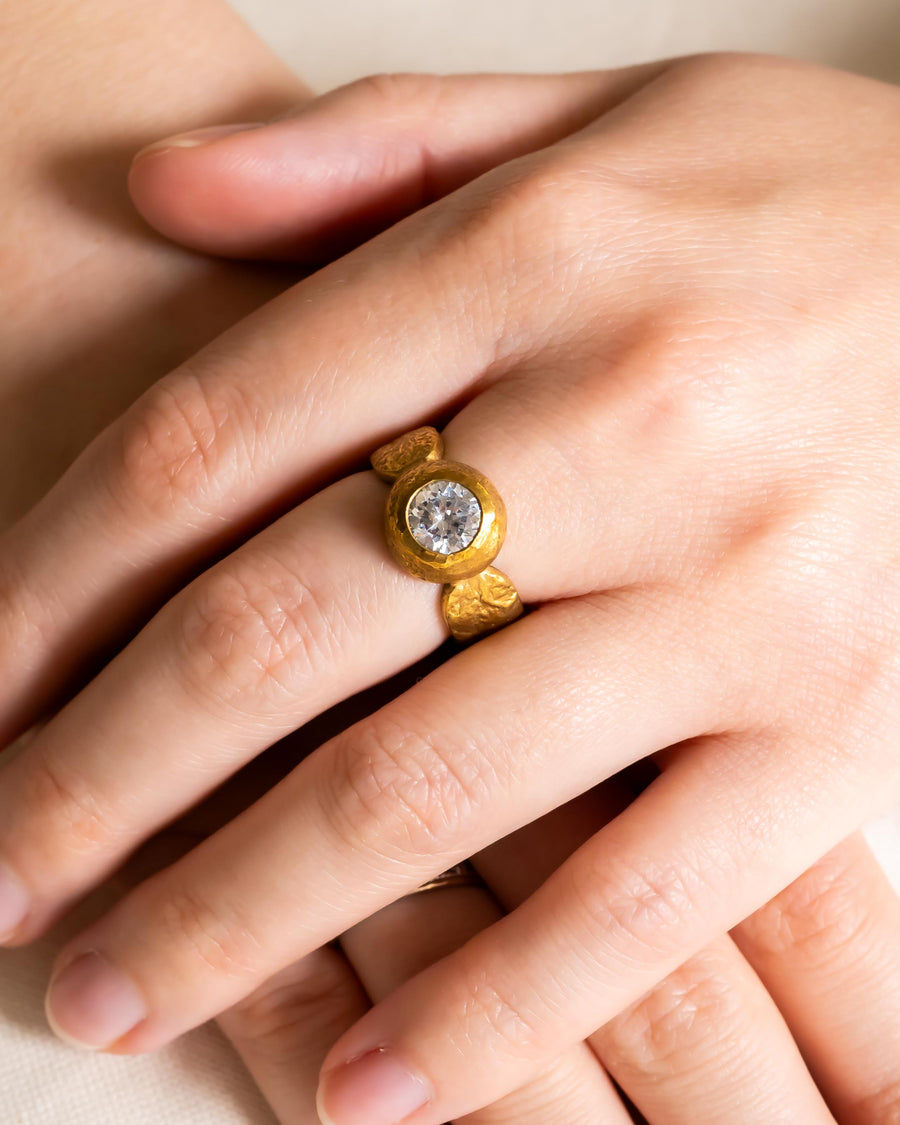 Gold nugget ring with a round diamond on a hand.