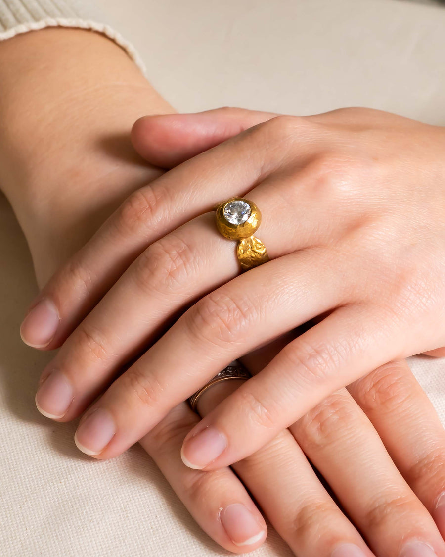 Gold nugget ring with a round diamond on a hand.