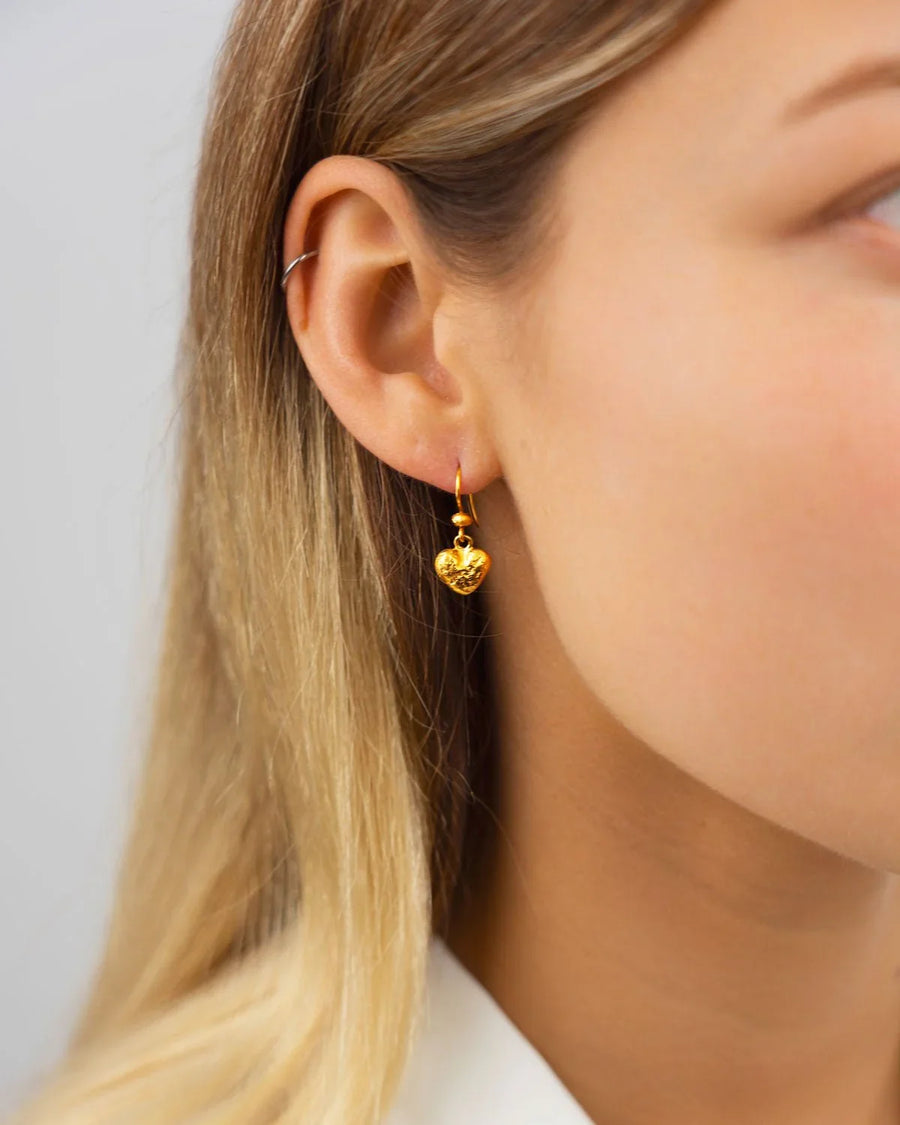 Gold nugget heart drop earring on a woman's ear.