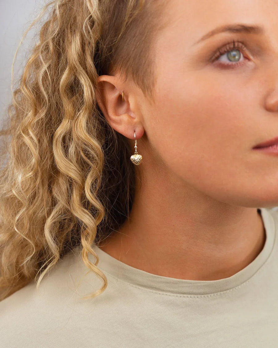 Gold nugget heart drop earring on a woman's ear.