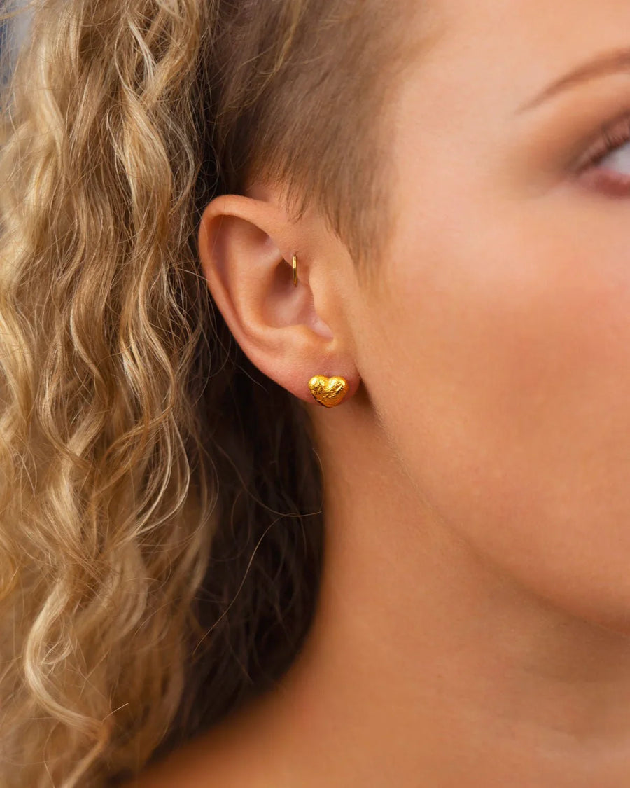 Gold nugget heart stud earring on an ear.
