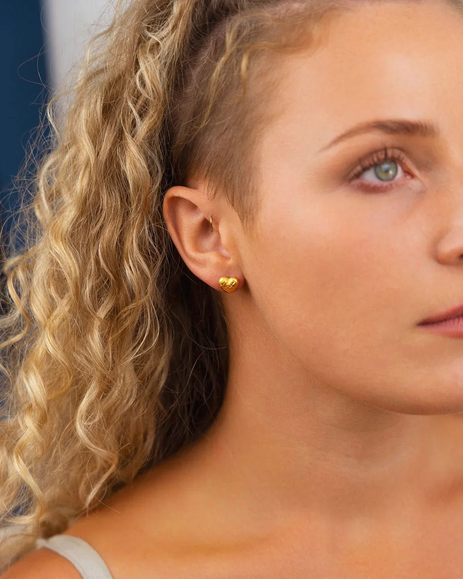 Gold nugget heart stud earring on a woman's ear.