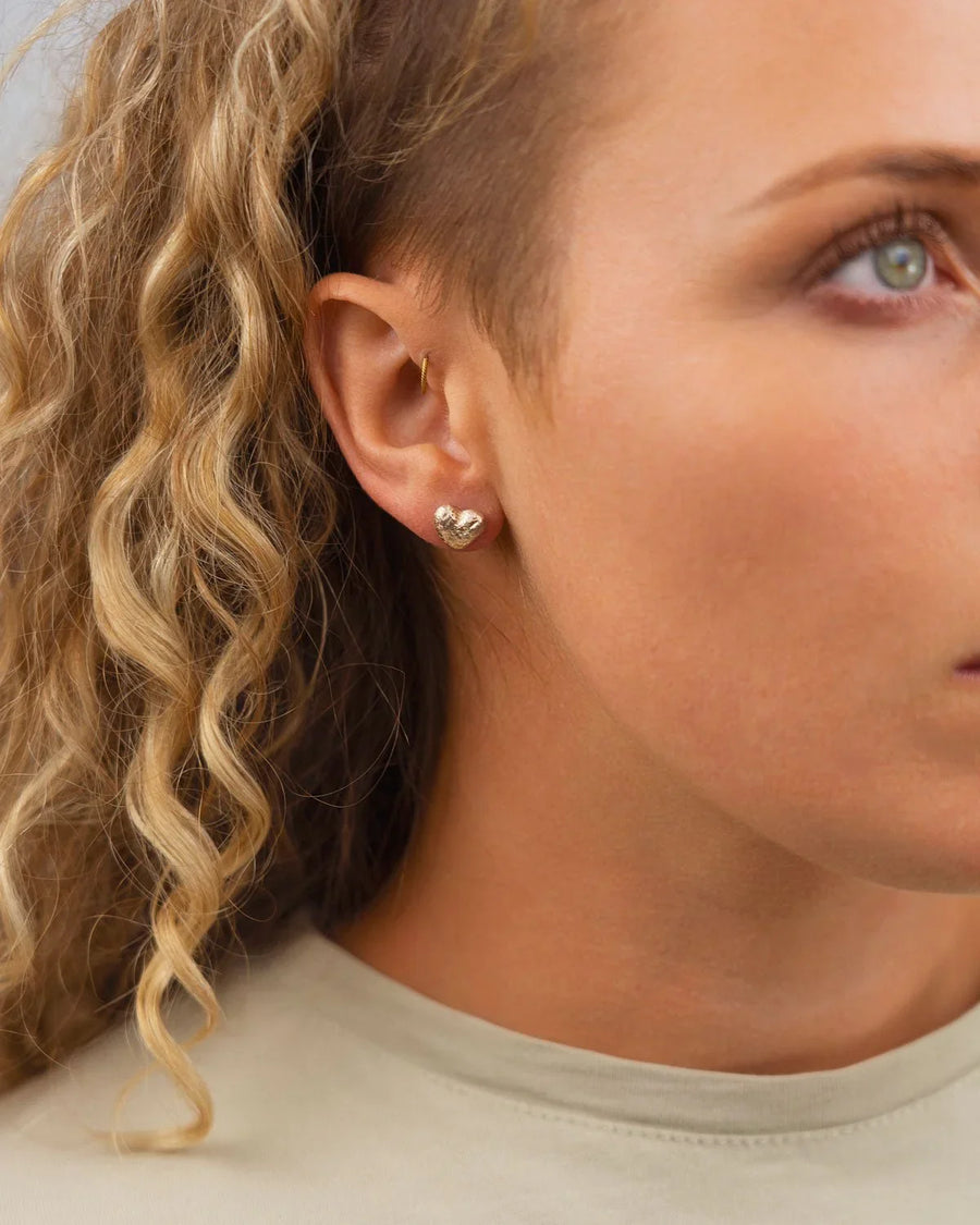 Gold nugget heart stud earring on a woman's ear.