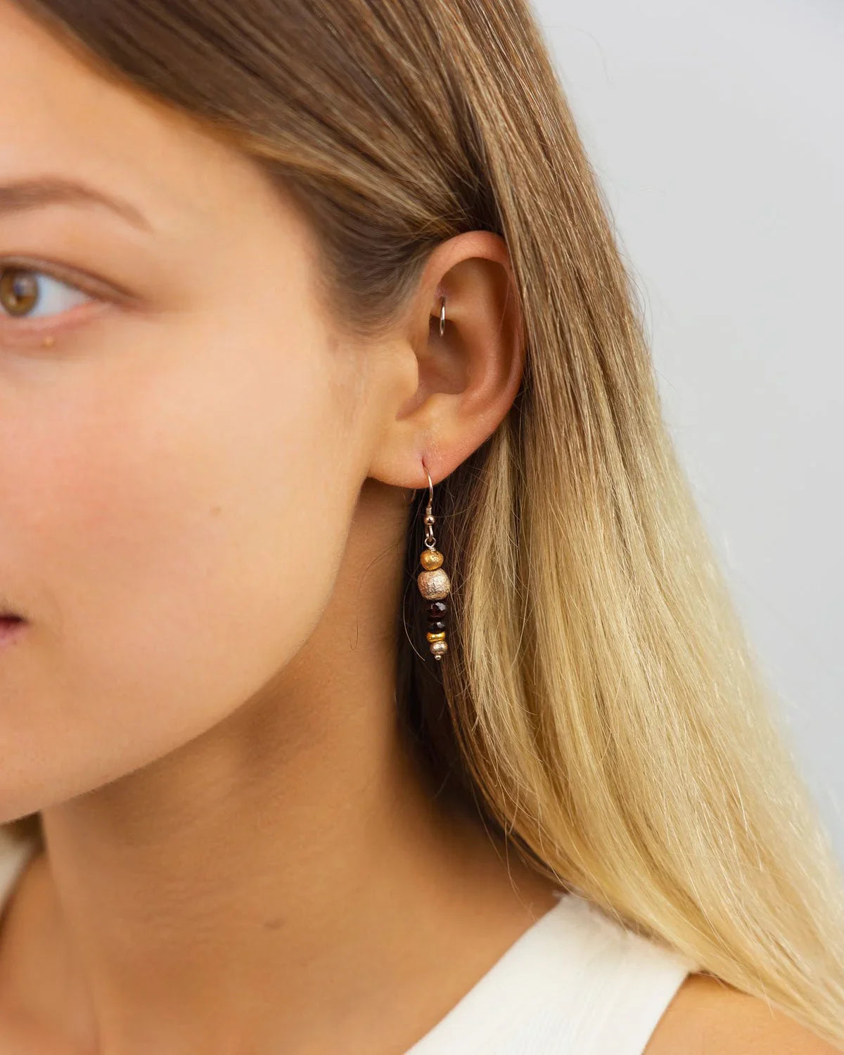 Faceted gemstone dangly earrings with gold accents worn on ear