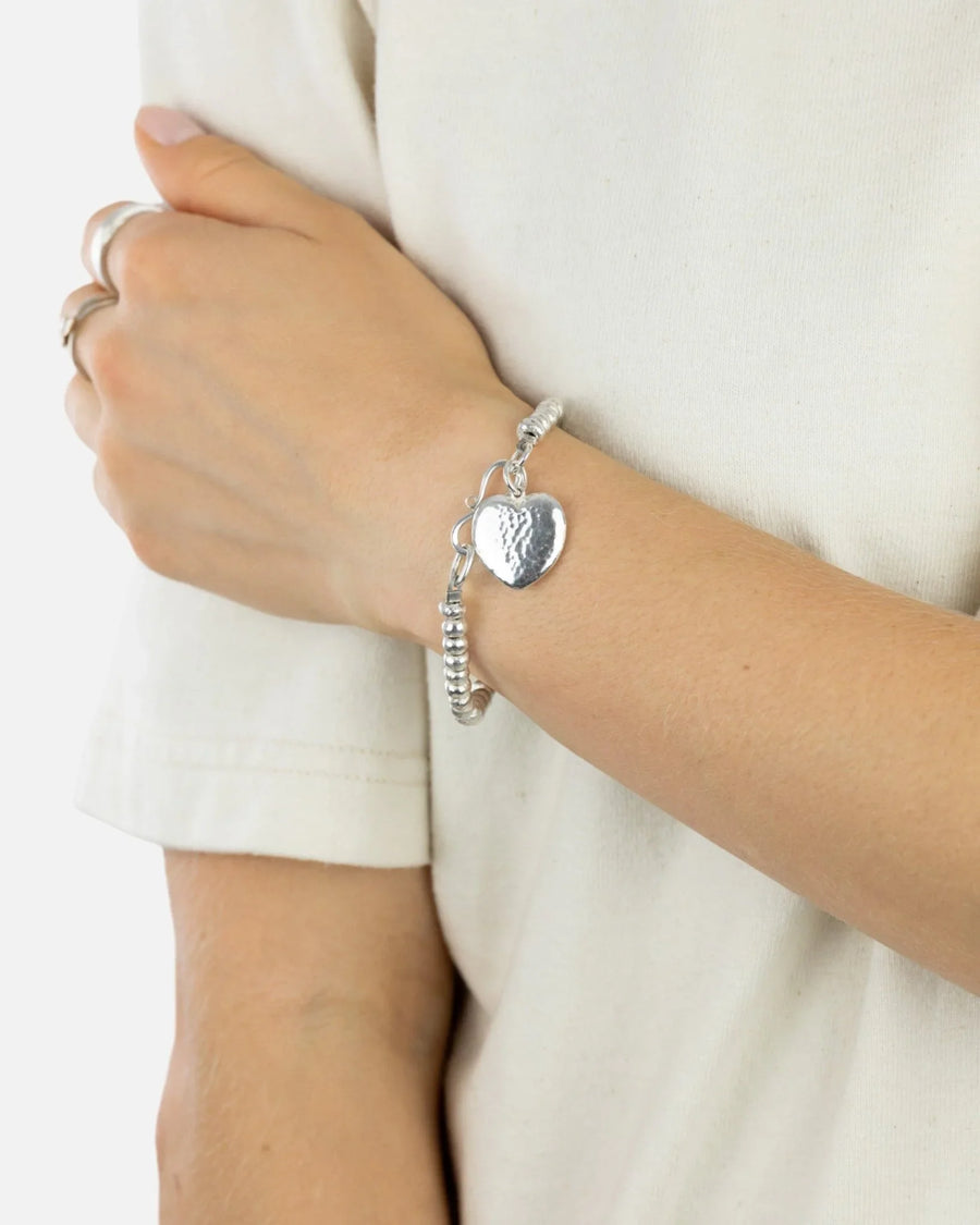 Hammered silver heart charm bracelet with beaded design worn on wrist