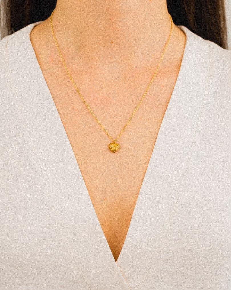 Gold nugget heart pendant on a delicate chain, worn on a white shirt.